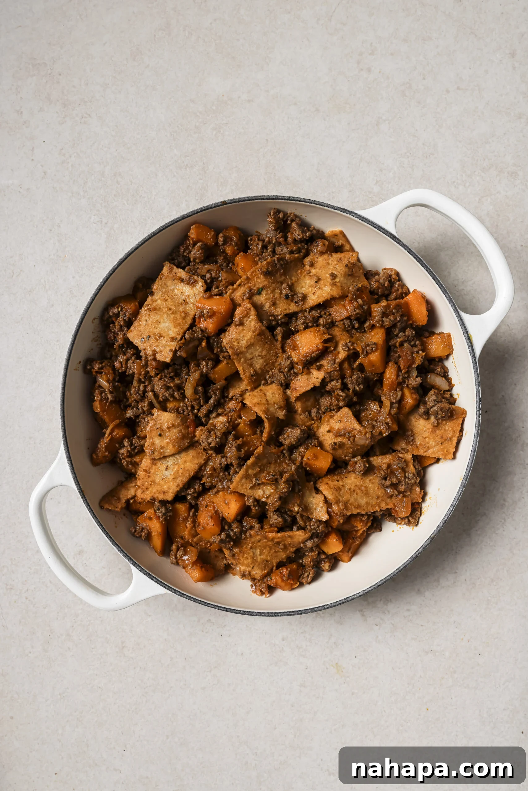 A large white pan with cooked ground beef, sweet potato and sliced tortillas.