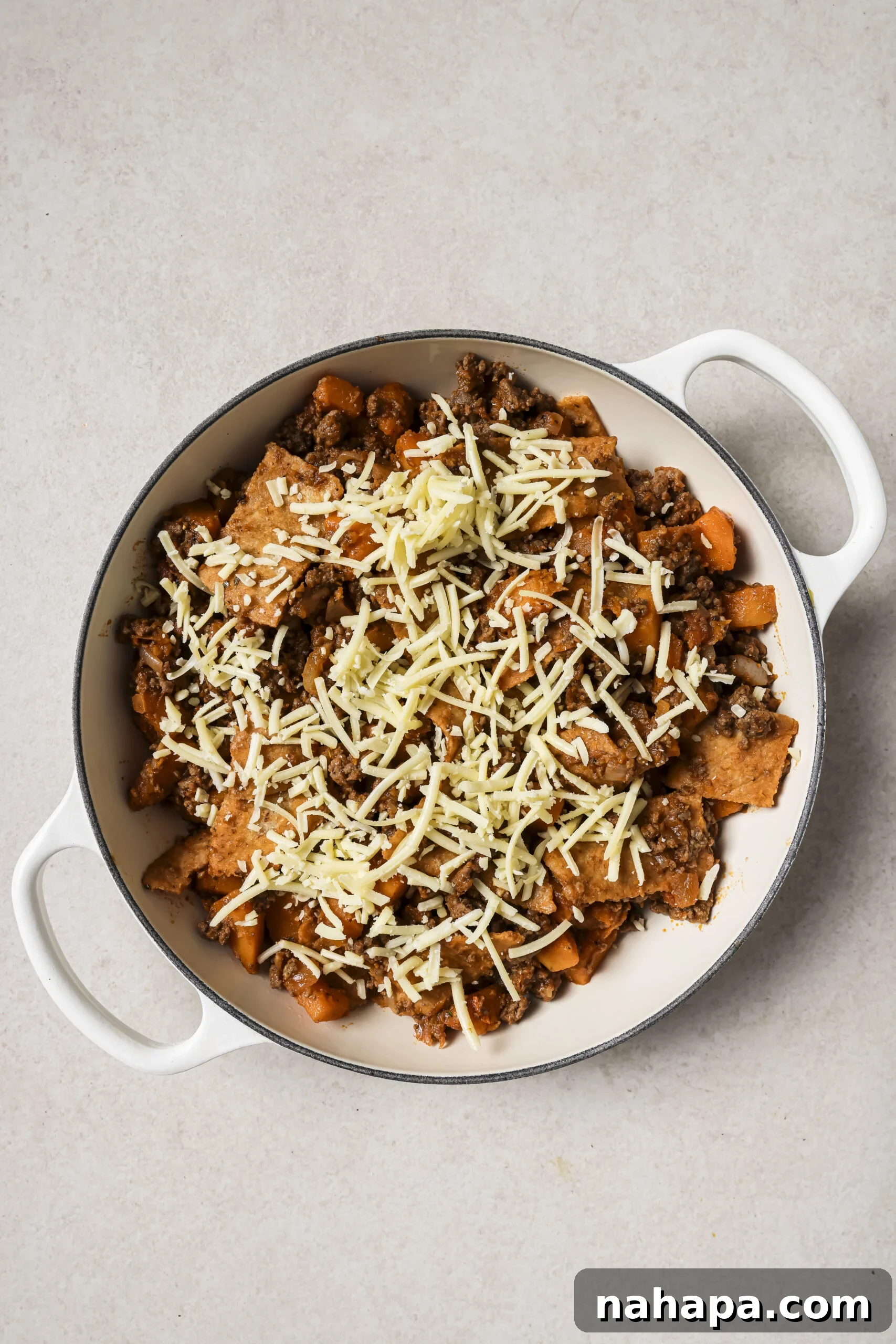 A large white pan with cooked ground beef, sweet potato, sliced tortillas and shredded cheese.