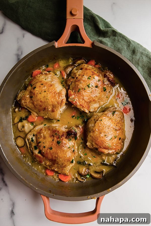 Top view of perfectly cooked chicken thighs simmering in a rich, golden sauce with mushrooms and carrots in a pan.