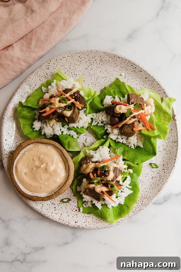 Close-up of fully assembled Hibachi steak lettuce wraps on a white plate, accompanied by a small cup of zesty mustard sauce.