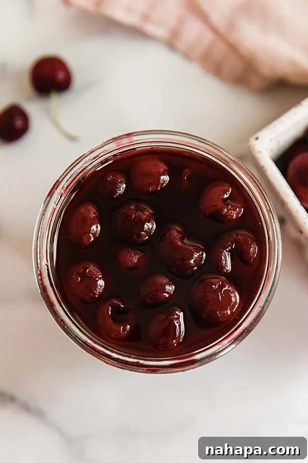 Top view of homemade maraschino cherries nestled in a glass jar, glistening in their rich syrup.
