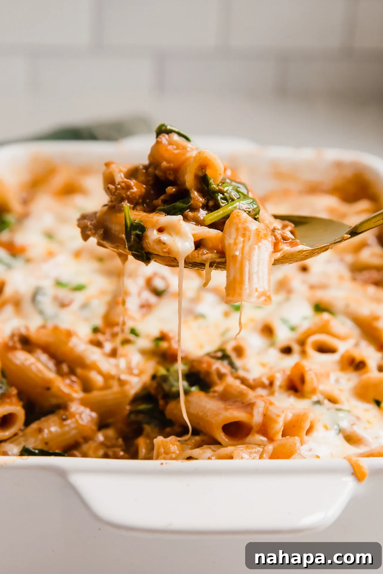 A large serving spoon scooping a portion of the gluten-free no-boil pasta bake from the ceramic dish. 