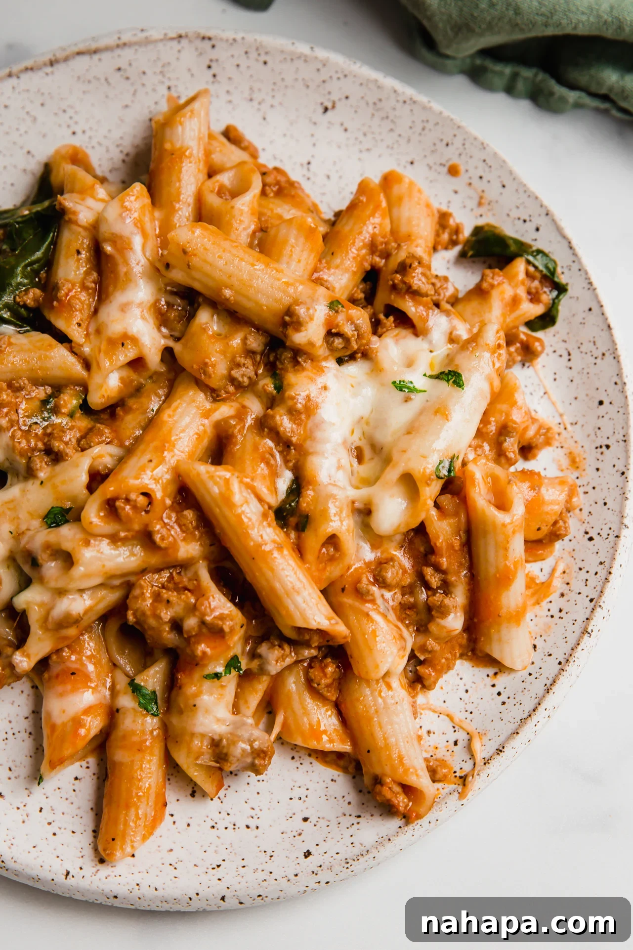 A serving of no boil pasta bake on a white plate, covered with melted cheese and a sprinkle of parsley. 