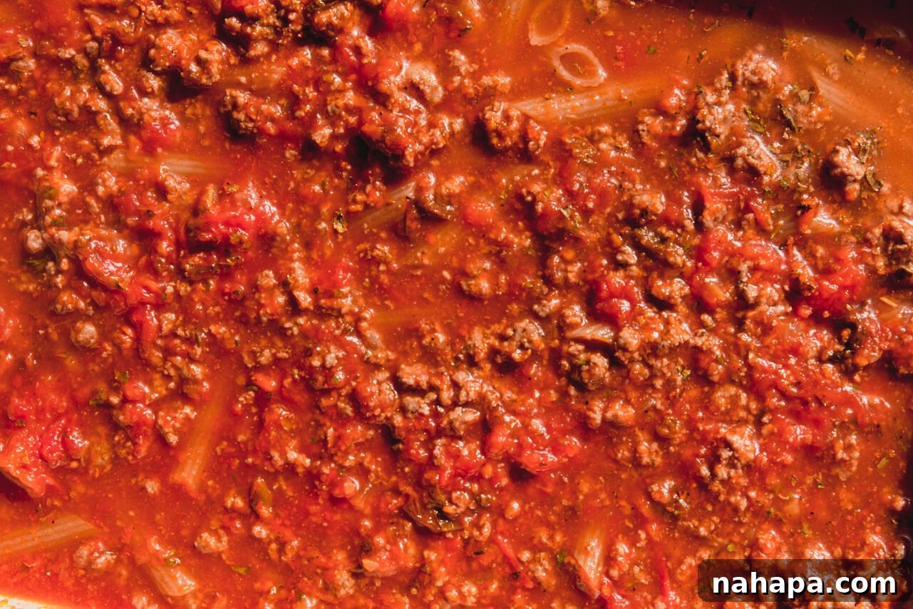 The ingredients in the baking dish are thoroughly stirred, ensuring pasta is submerged in liquid. Covered dish ready for baking.
