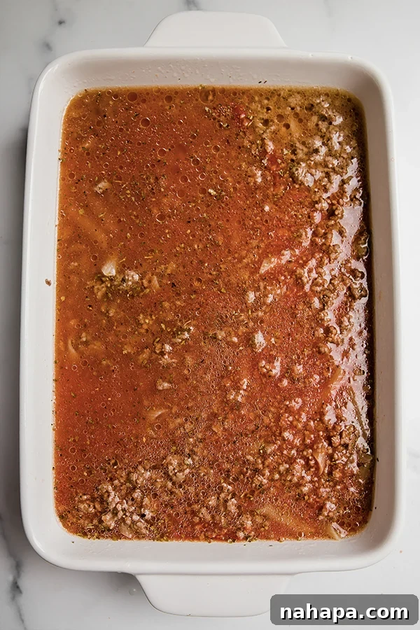 Ultimate No Boil Gluten Free Bacon Cheeseburger Pasta Bake 3 A casserole dish filled with uncooked gluten-free pasta, ground beef, tomato sauce, and broth, ready to be stirred.