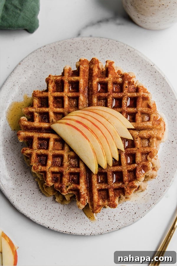 Wholesome Apple Waffles Gluten Free Paleo Vegan 4 A beautifully arranged stack of gluten-free apple waffles, garnished with thin apple slices and a generous drizzle of maple syrup, on a rustic plate.