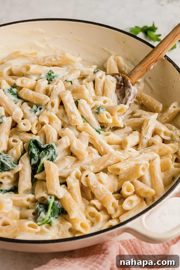 A pot of Easy Penne Alfredo with a wooden spoon in it.