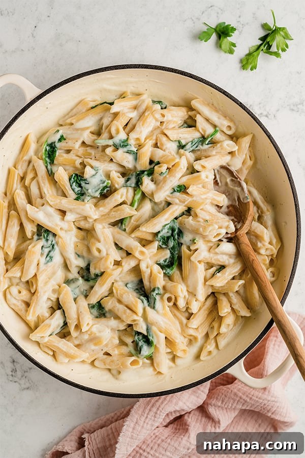 A pot of Easy Penne Alfredo with a wooden spoon in it.