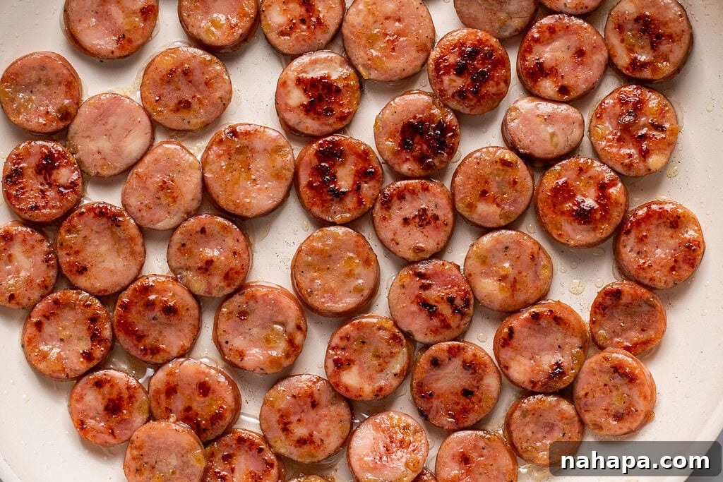 Close-up of golden-brown sliced chicken apple sausage cooking in a skillet, showing a delicious sear.