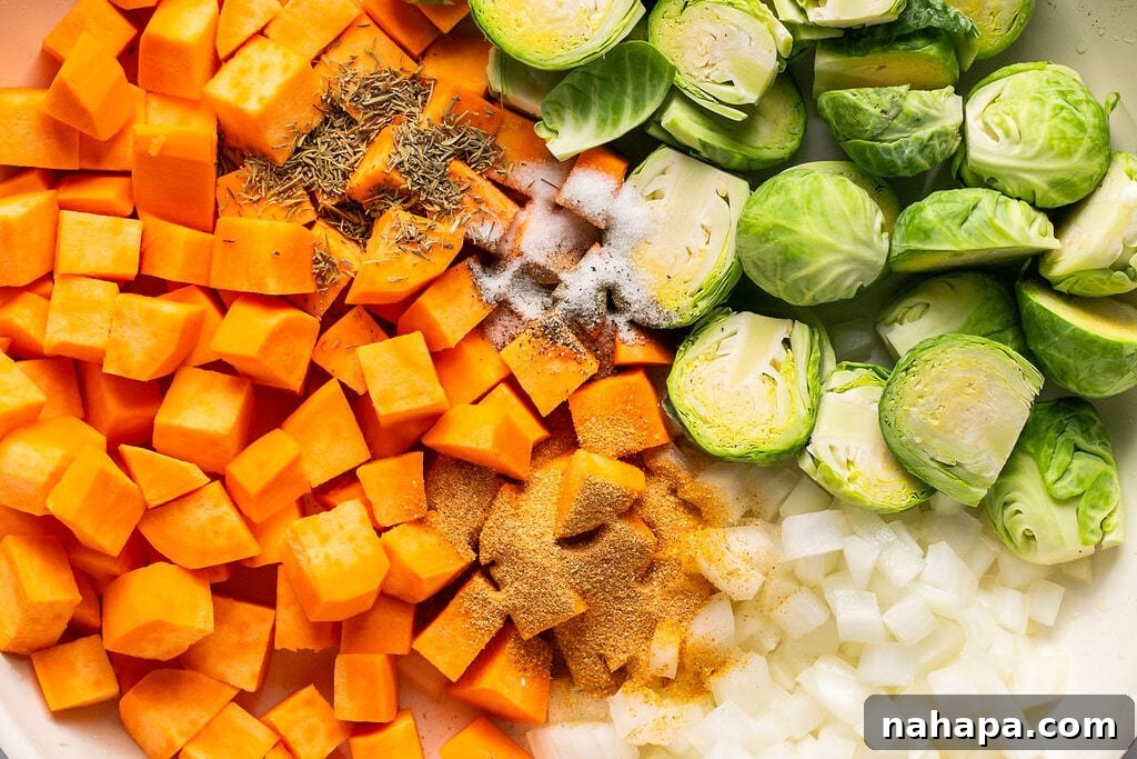 Raw diced sweet potato, halved Brussels sprouts, and diced onion in a skillet, ready to be cooked.