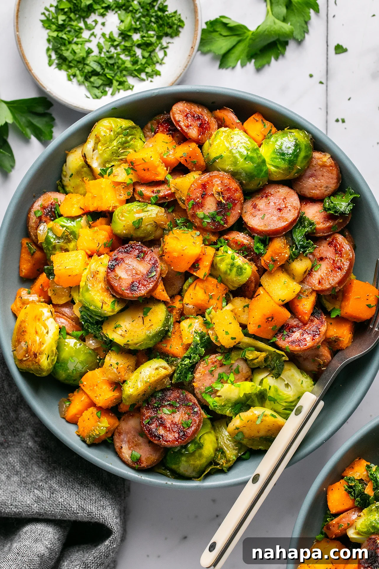 A vibrant close-up of the finished apple chicken sausage and vegetable skillet in a large white bowl, garnished with fresh parsley.