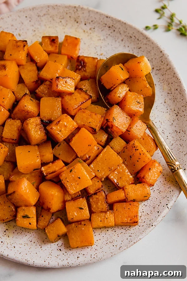 Air-fried butternut squash cubes artfully arranged on a white plate with a serving spoon, garnished with fresh thyme.
