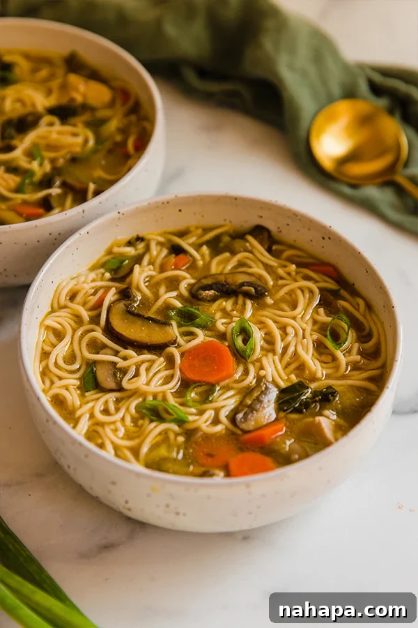 Umami-Rich Asian Chicken Noodle Soup 3 Two bowls of Asian Inspired Chicken Noodle Soup on a wooden counter, ready to be served.
