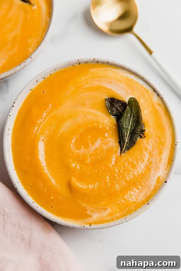 A bowl of roasted acorn squash soup garnished with fresh sage leaves and a drizzle of coconut milk.