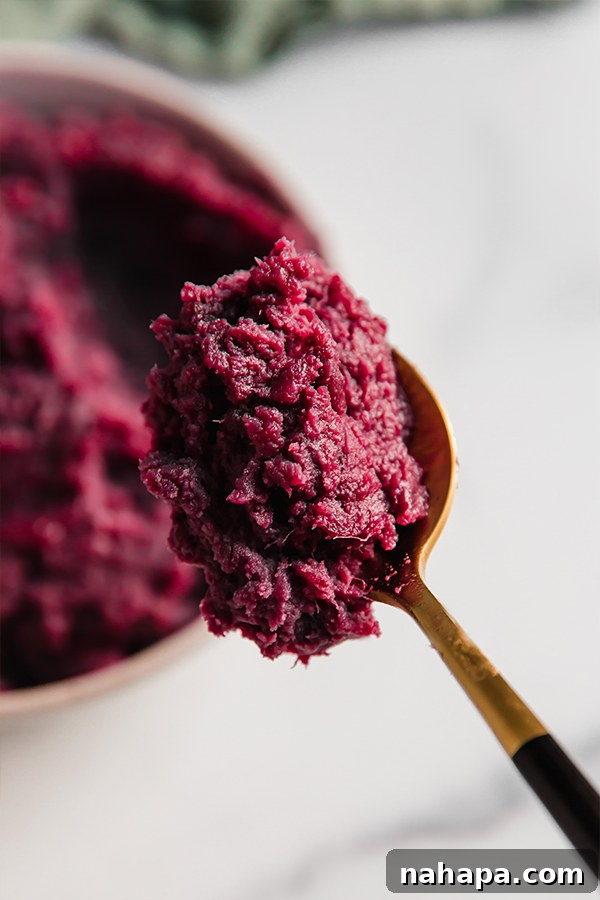 A spoon scooping a portion of fluffy purple mashed sweet potatoes.