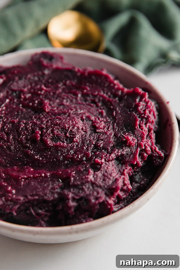 A close-up of a serving bowl filled with creamy purple mashed sweet potatoes, garnished lightly.