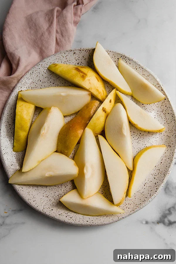 A close-up shot of freshly sliced Bartlett pears on a white plate, ready for caramelization.