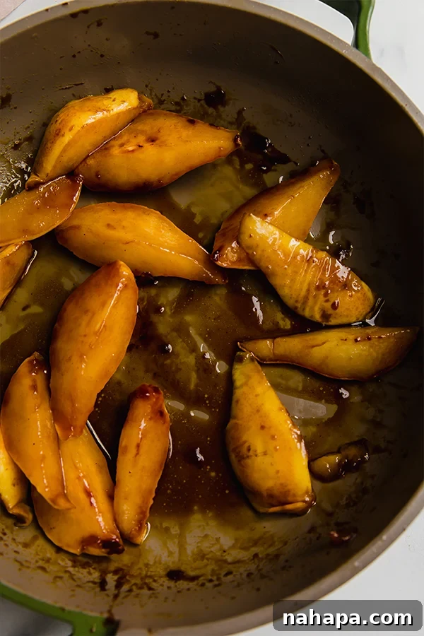 Pear slices cooking gently in a skillet with melted ghee, beginning to caramelize.