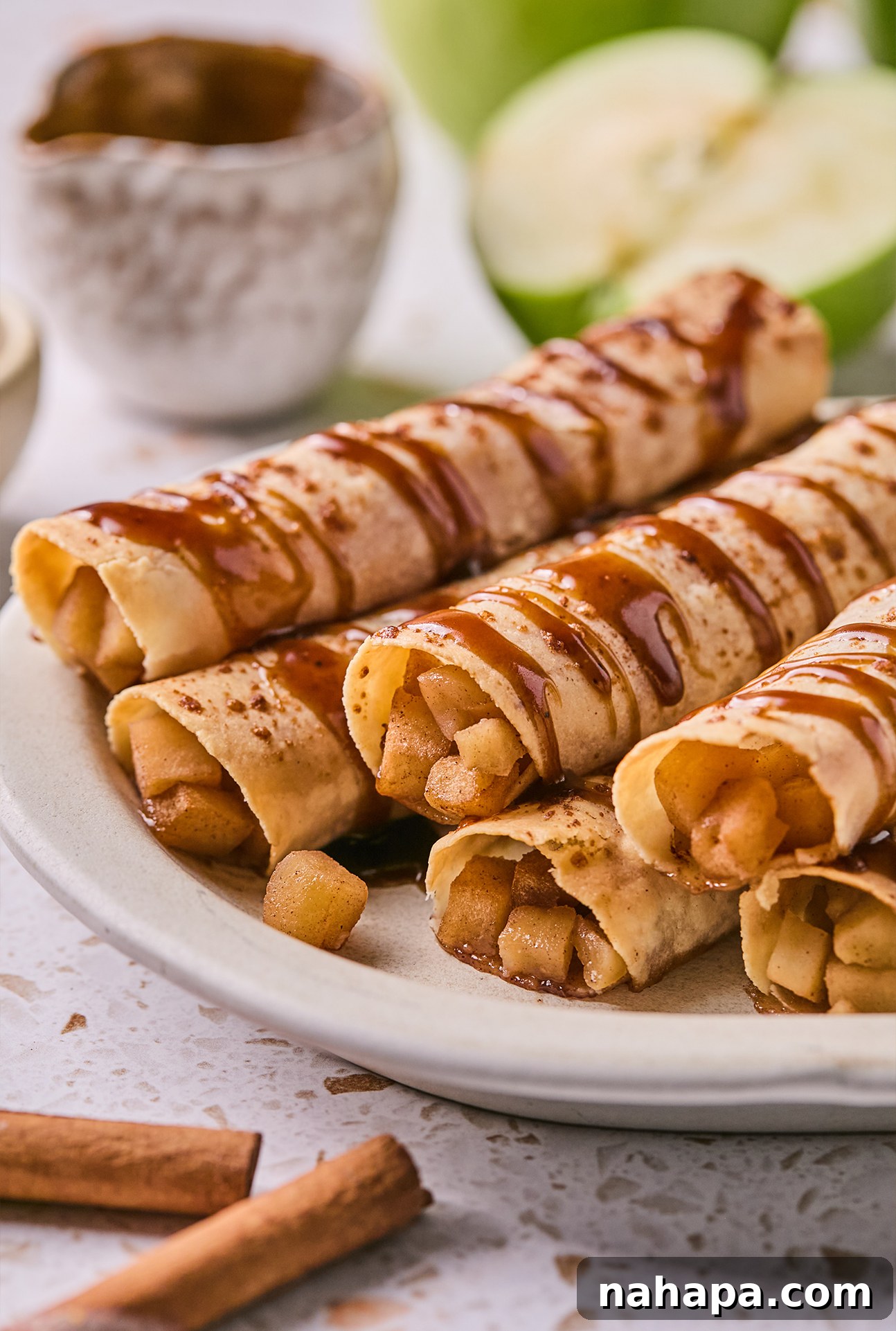 Apple Cinnamon Swirls Gluten Free 12 Apple pie roll ups on a plate drizzled with caramel, and with extra caramel on the side.