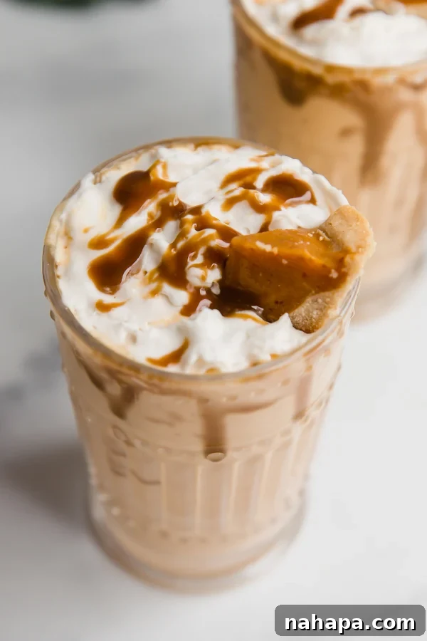 Two pumpkin pie milkshakes in elegant glasses, topped with whipped cream and a mini slice of pumpkin pie.