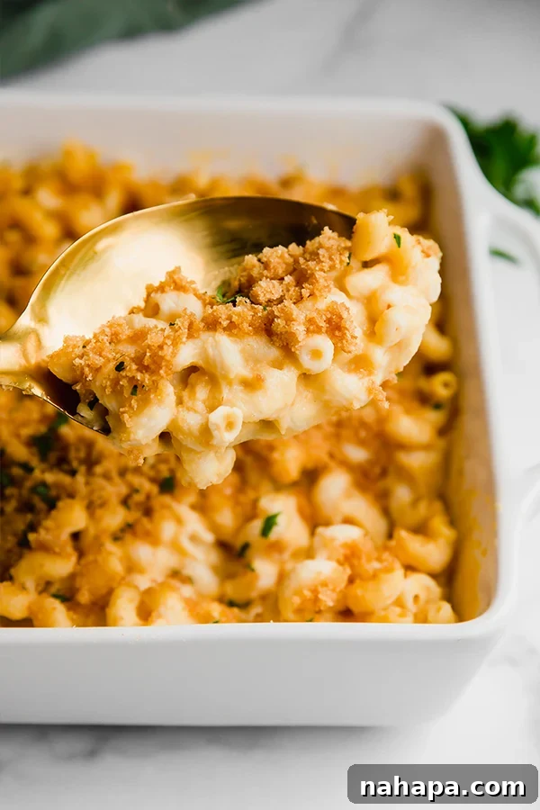 Indulgent Paleo Baked Mac and Cheese Gluten Dairy Free 4 A spoon digging into a dish of mac and cheese, showing its creamy texture and crispy topping.