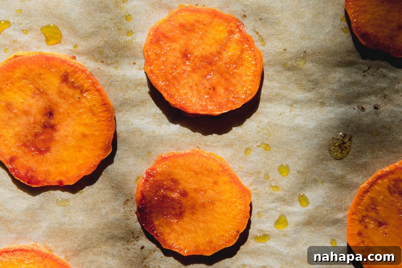 Baked sweet potato slices, tender and slightly browned, on a baking sheet.