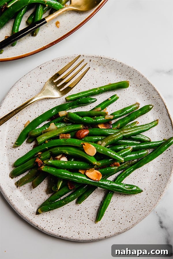 A serving plate generously piled with green beans, adorned with glistening bacon bits and golden toasted almonds.