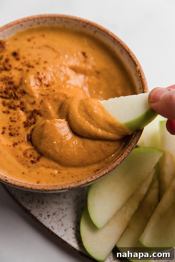 A sliced red apple being dipped into a luscious bowl of homemade pumpkin pie dip, illustrating its perfect dipping consistency.