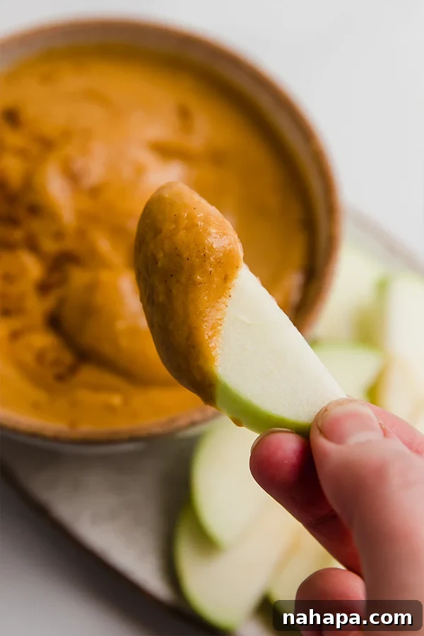 A vibrant red apple segment generously coated in creamy pumpkin pie dip, ready to be eaten, highlighting the dip's rich texture.