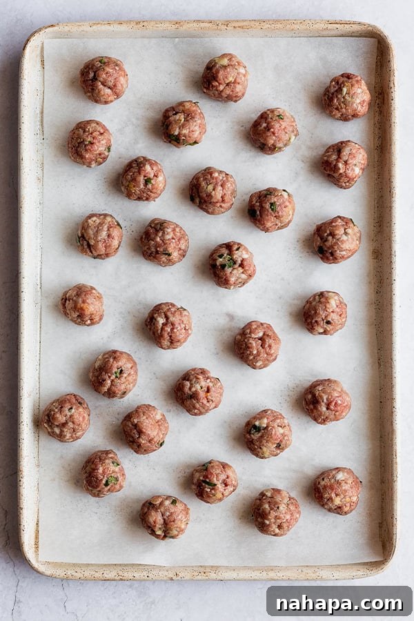 Small, perfectly formed meatballs waiting on a baking sheet before being cooked for the soup.
