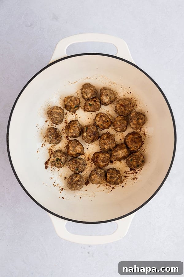 Golden-brown meatballs simmering in a Dutch oven, adding rich flavor to the soup base.