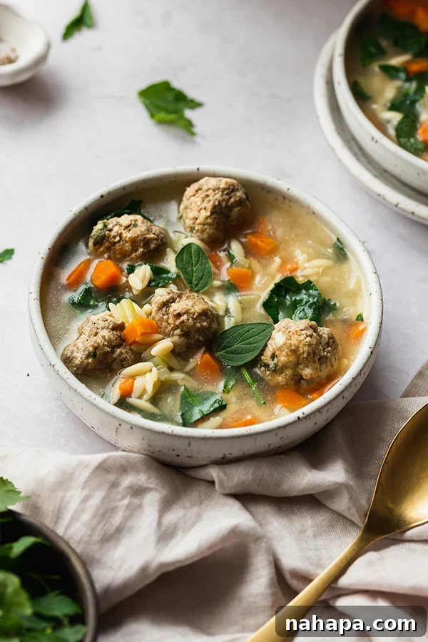 A close-up of a steaming bowl of Italian Wedding Soup, showcasing the tender meatballs, vibrant spinach, and delicate orzo.