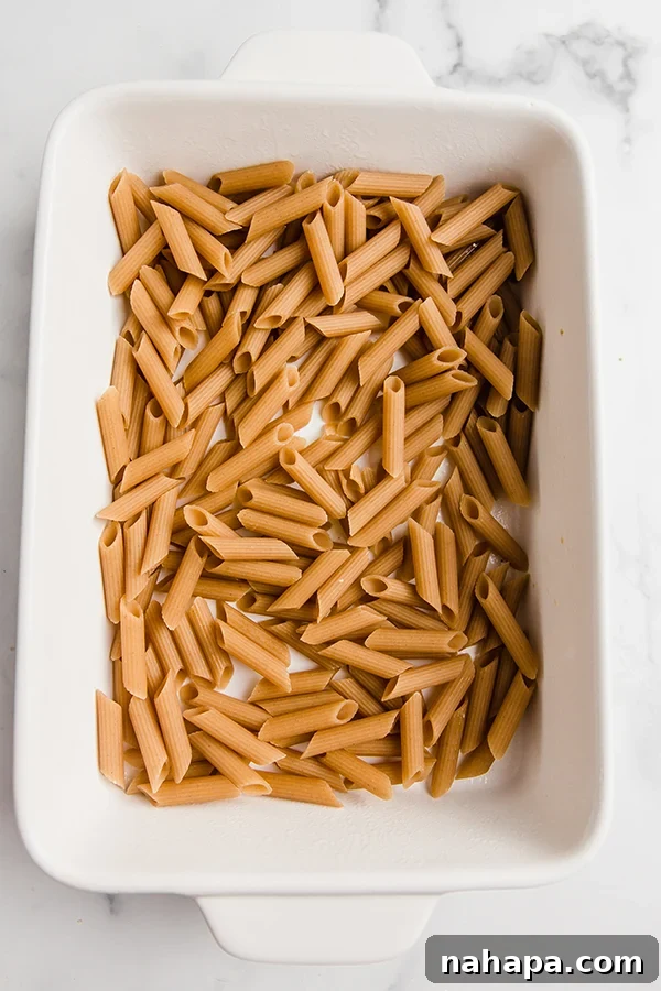Uncooked gluten-free pasta and cooked chicken seasoned and mixed in a baking dish, waiting for the sauce.