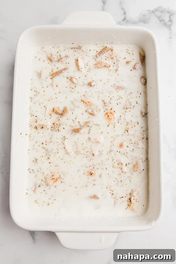 The baking dish filled with uncooked pasta, chicken, and rich cauliflower alfredo sauce, prior to baking.