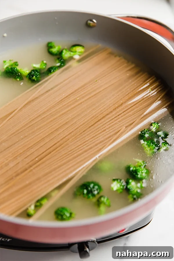 Easy One-Pot Lemon Chicken Pasta Gluten Free Dairy Free 4 A wide, deep pot containing spaghetti, broccoli, and broth, ready for cooking.