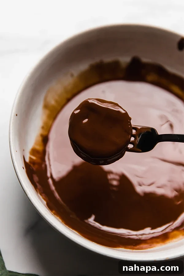 A chocolate sandwich cookie being carefully dipped into a bowl of melted chocolate, ensuring a full and even coating.