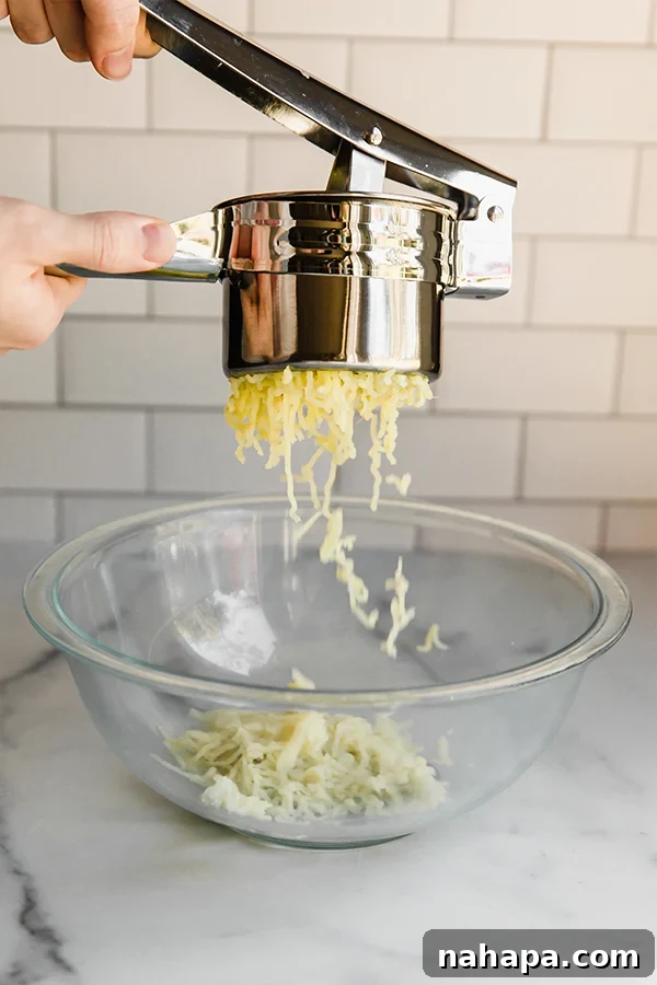 Paleo AIP Sweet Potato Lefse: A Healthy Norwegian Delight 3 Warm, cooked white sweet potato being pressed through a potato ricer into a clear glass mixing bowl, creating a fine, smooth mash.