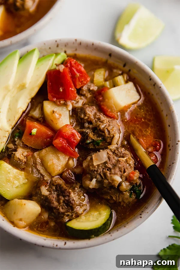 A vibrant bowl of Albondigas soup, garnished with fresh cilantro and avocado slices.