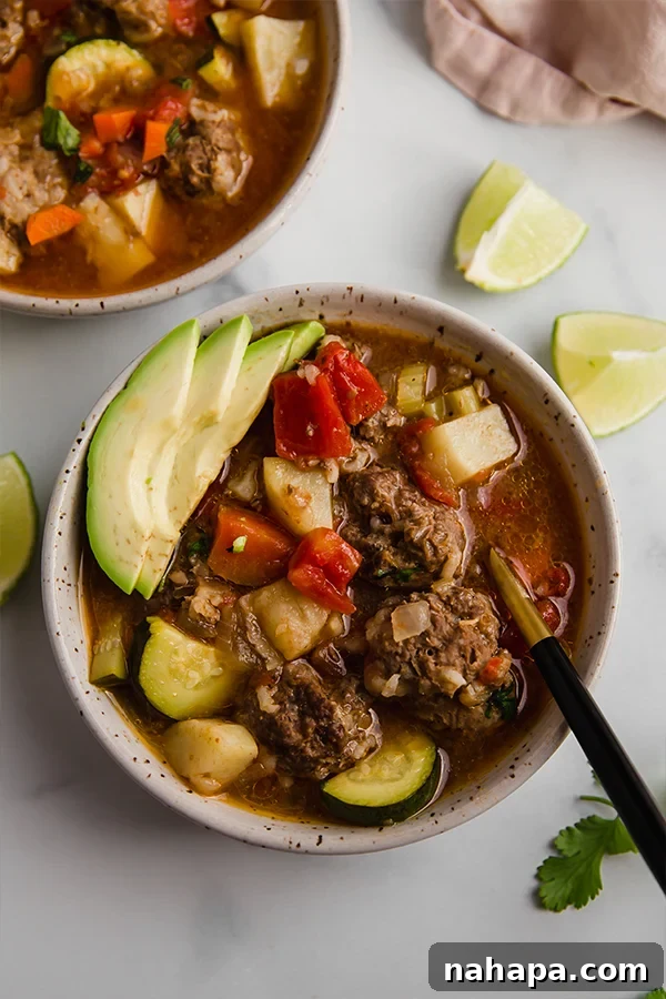 A close-up shot of a bowl of Albondigas soup with a spoon, showing the hearty contents.