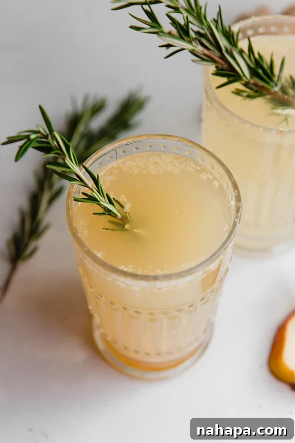 Ginger Pear Fizz 2 A glass of sparkling ginger pear mocktail with a rosemary garnish, set against a warm, inviting background.