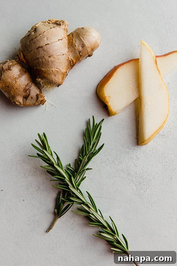 Ginger Pear Fizz 3 Ingredients for sparkling ginger pear mocktail laid out on a table: fresh ginger, pear juice, honey, sparkling water, and rosemary sprigs.