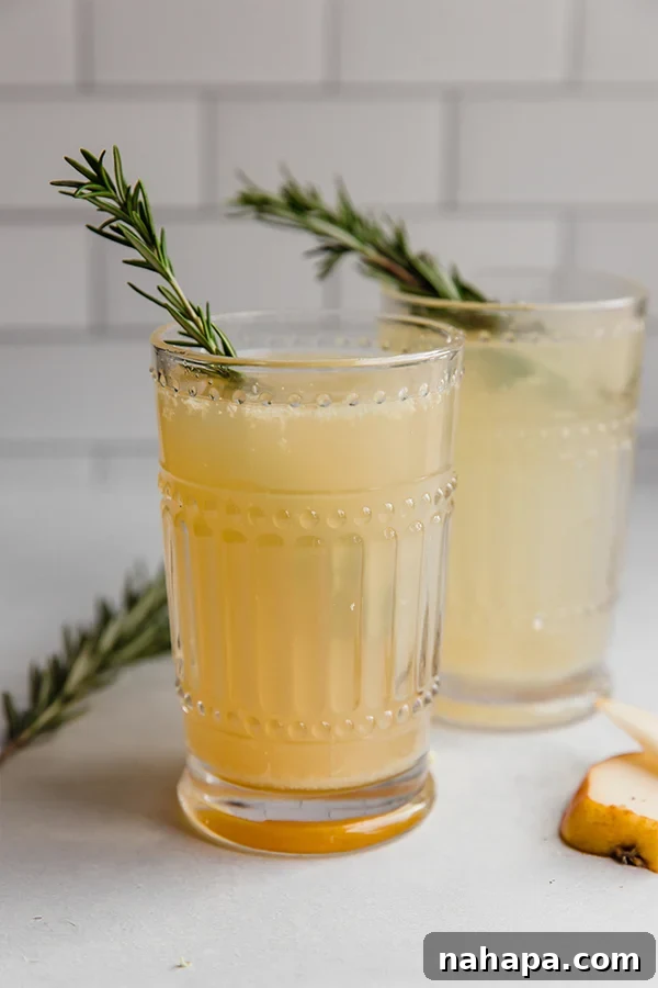 Ginger Pear Fizz 4 Two ginger pear mocktails in elegant glasses, garnished with fresh rosemary sprigs, against a clean white background.