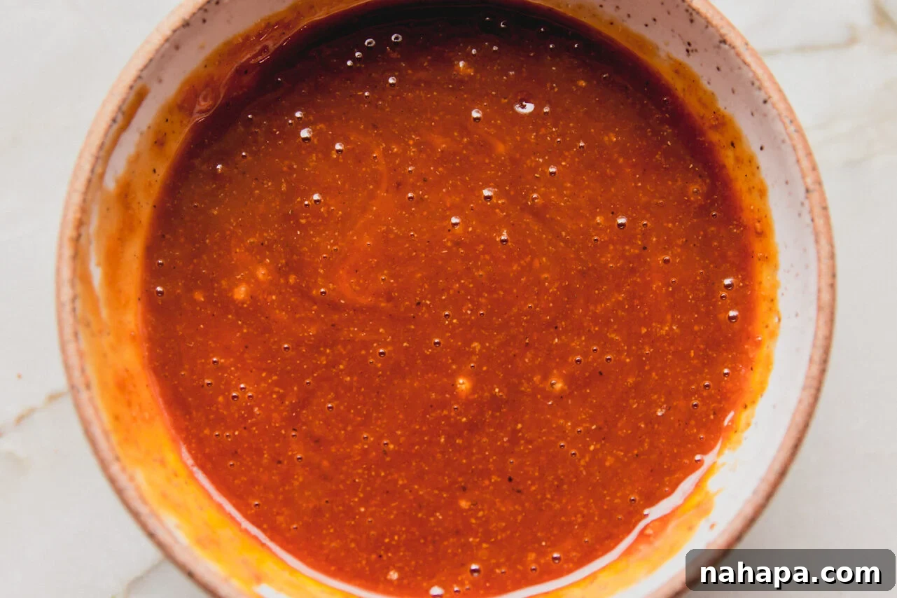 The firecracker sauce ingredients are now thoroughly whisked together in the bowl, creating a smooth, cohesive liquid that is ready to use.