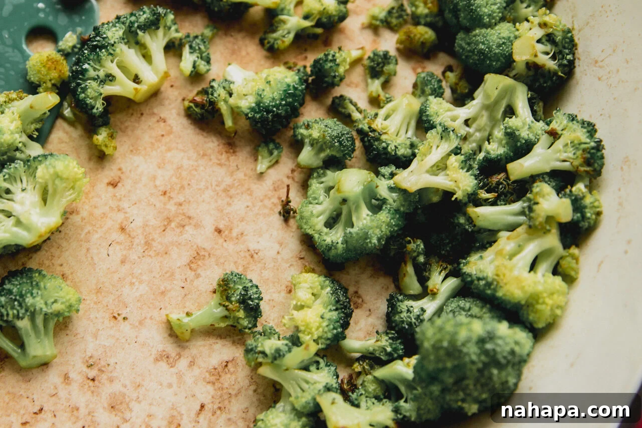 Broccoli florets are being sautéed in a large non-stick pan over medium heat, showing slight charring and a vibrant green color as they cook.