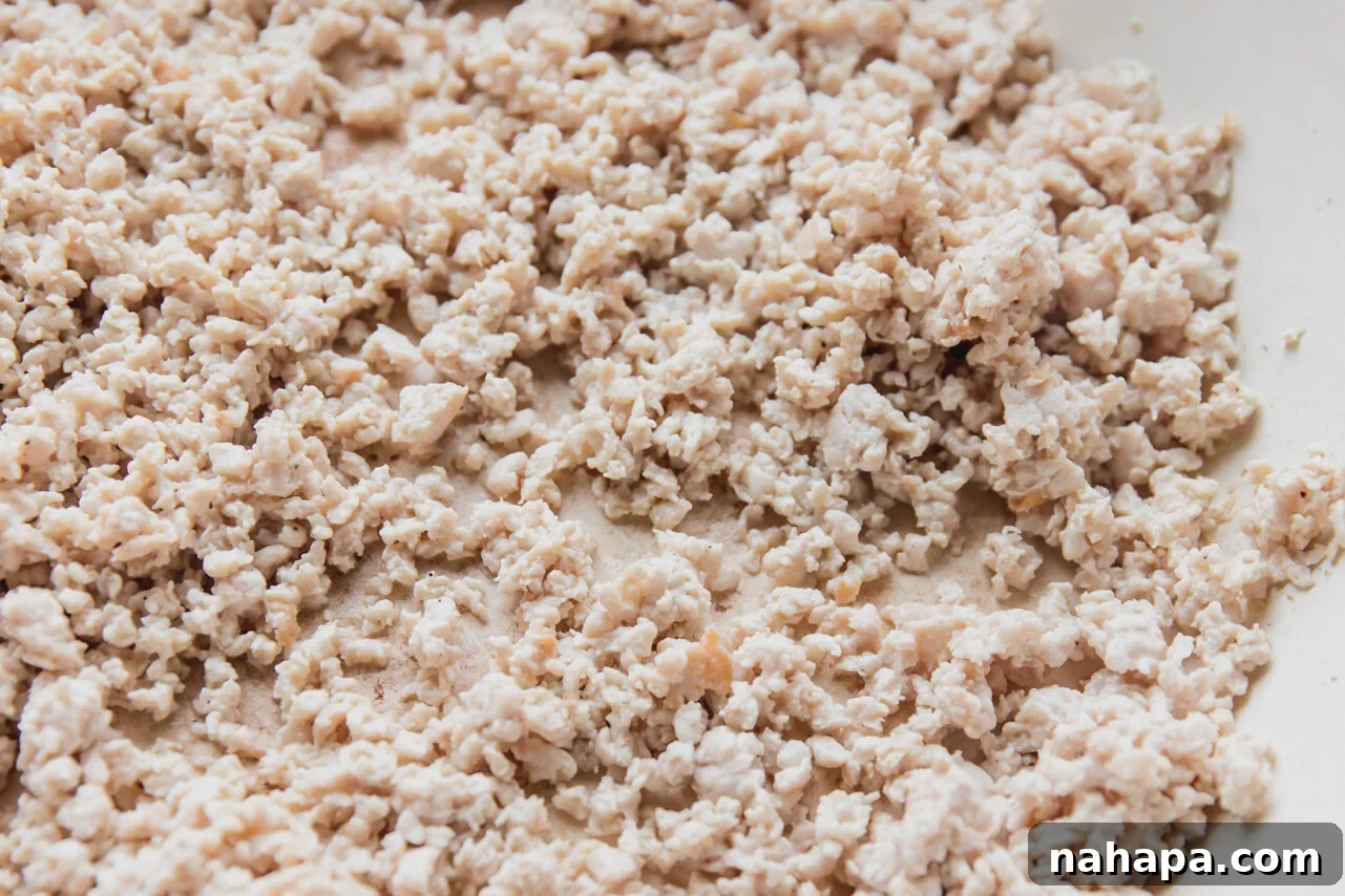 Lean ground chicken is cooking in the same large pan, being broken apart with a spatula as it browns evenly, indicating it's nearly cooked through.