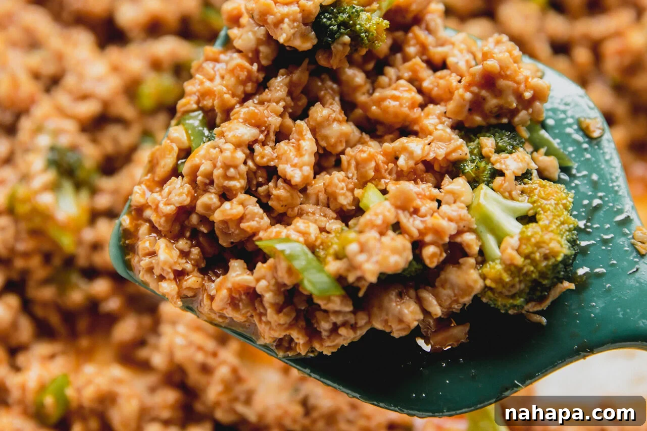 A green spatula is scooping a portion of the fully cooked Firecracker Ground Chicken and broccoli mixture from the pan, illustrating the final steps before serving.