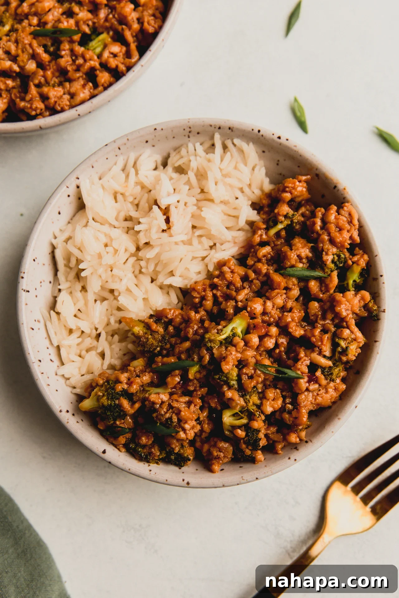 A beautifully presented Firecracker Ground Chicken Bowl, garnished with sesame seeds and fresh green onions, with the vibrant colors of chicken and broccoli clearly visible against a bed of rice.