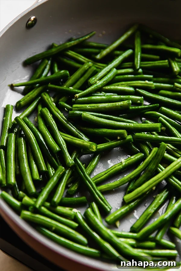 Green beans and garlic sizzling in a large skillet, midway through the sautéing process.