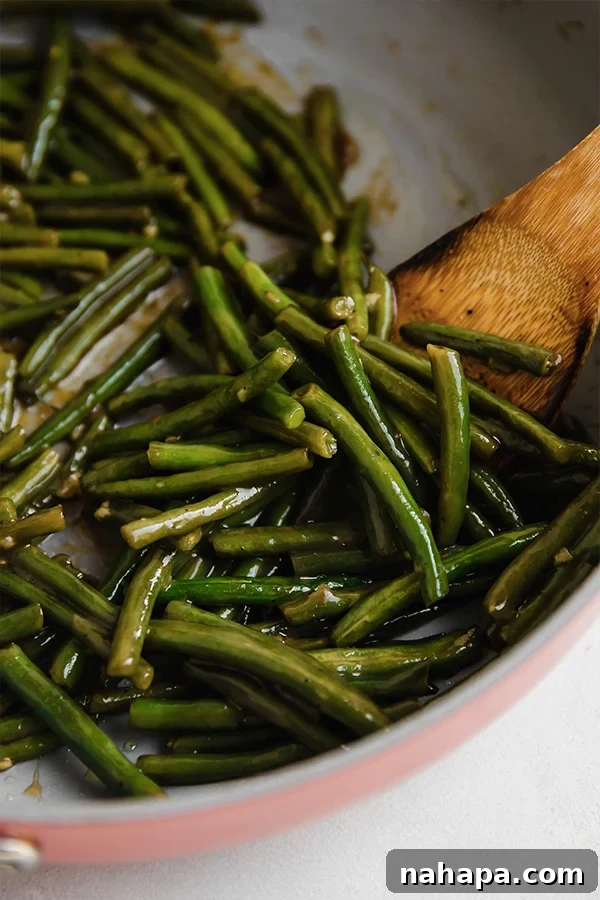 Green beans simmering in the sweet and sour sauce in a skillet, appearing glossy and well-coated.