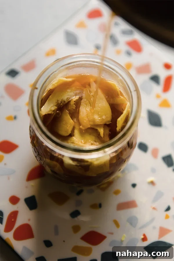 Hot pickling liquid being poured over thinly sliced ginger in a glass jar, submerging the ginger completely.